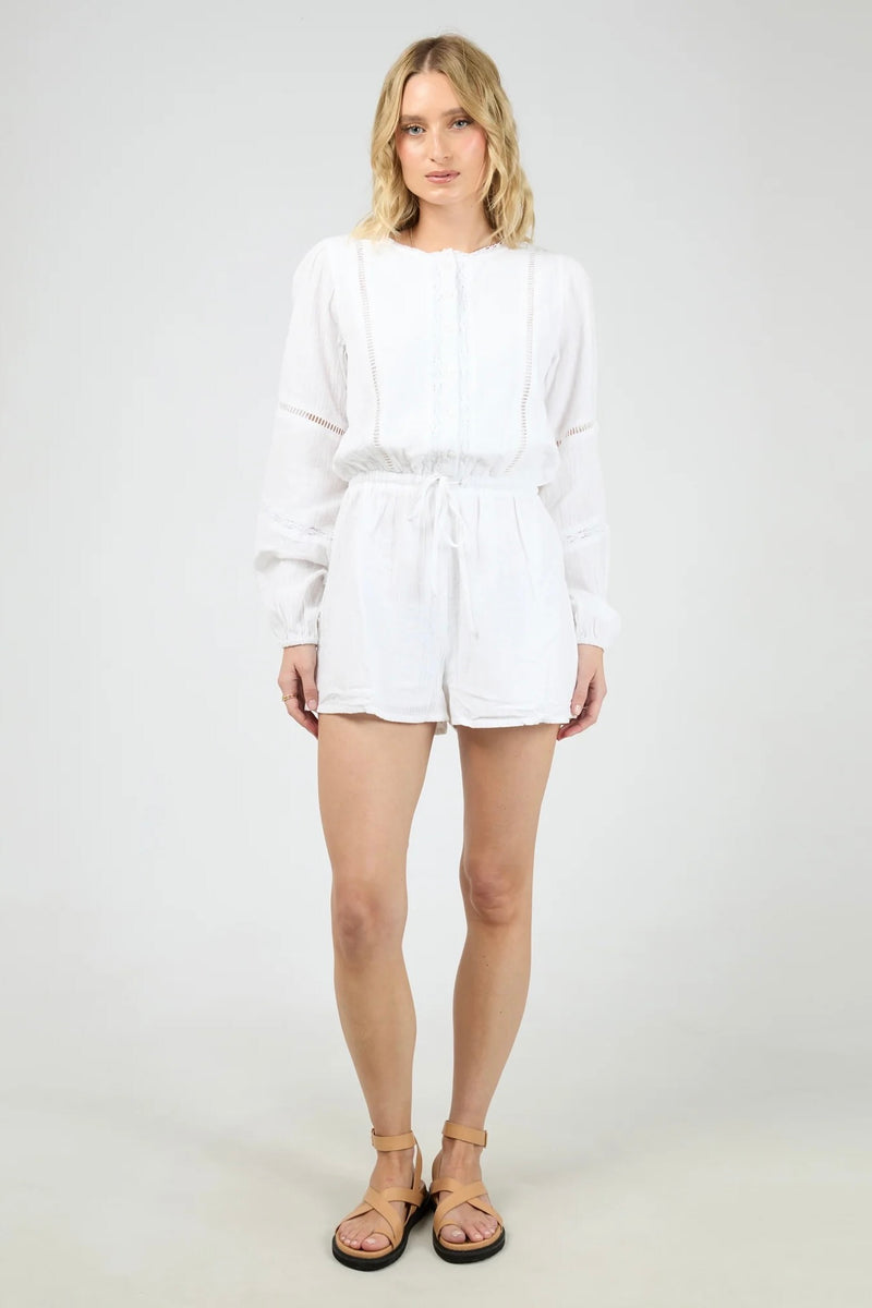 Model wearing the All About Eve Dusty Playsuit in white, featuring long sleeves, lace detailing, and a drawstring waist.