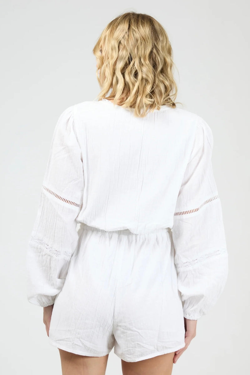 Model wearing the All About Eve Dusty Playsuit in white, featuring long sleeves, lace detailing, and a drawstring waist.