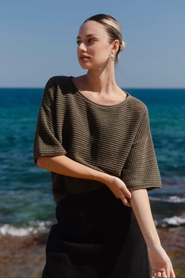 Woman wearing Re:Union The Label Sunrise Khaki SS Crochet Knit Top in crochet knit with short sleeves, relaxed fit, and round neckline, styled with denim jeans.
