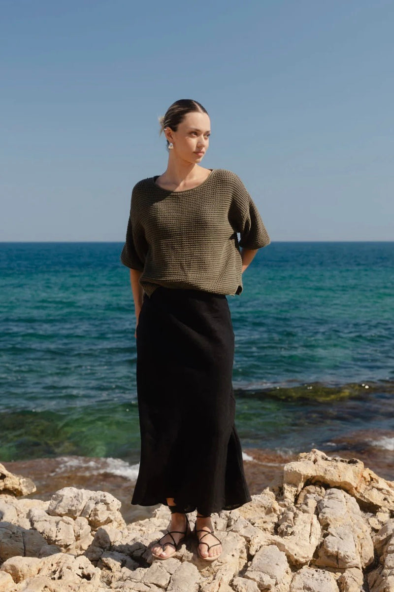 Woman wearing Re:Union The Label Sunrise Khaki SS Crochet Knit Top in crochet knit with short sleeves, relaxed fit, and round neckline, styled with denim jeans.