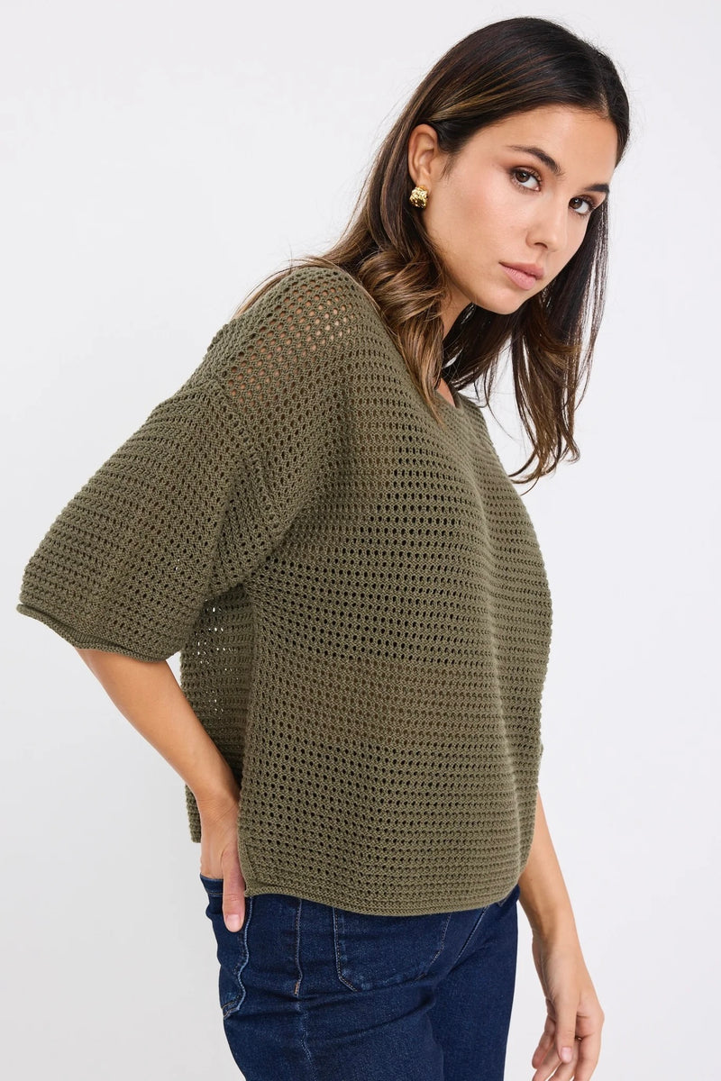 Woman wearing Re:Union The Label Sunrise Khaki SS Crochet Knit Top in crochet knit with short sleeves, relaxed fit, and round neckline, styled with denim jeans.