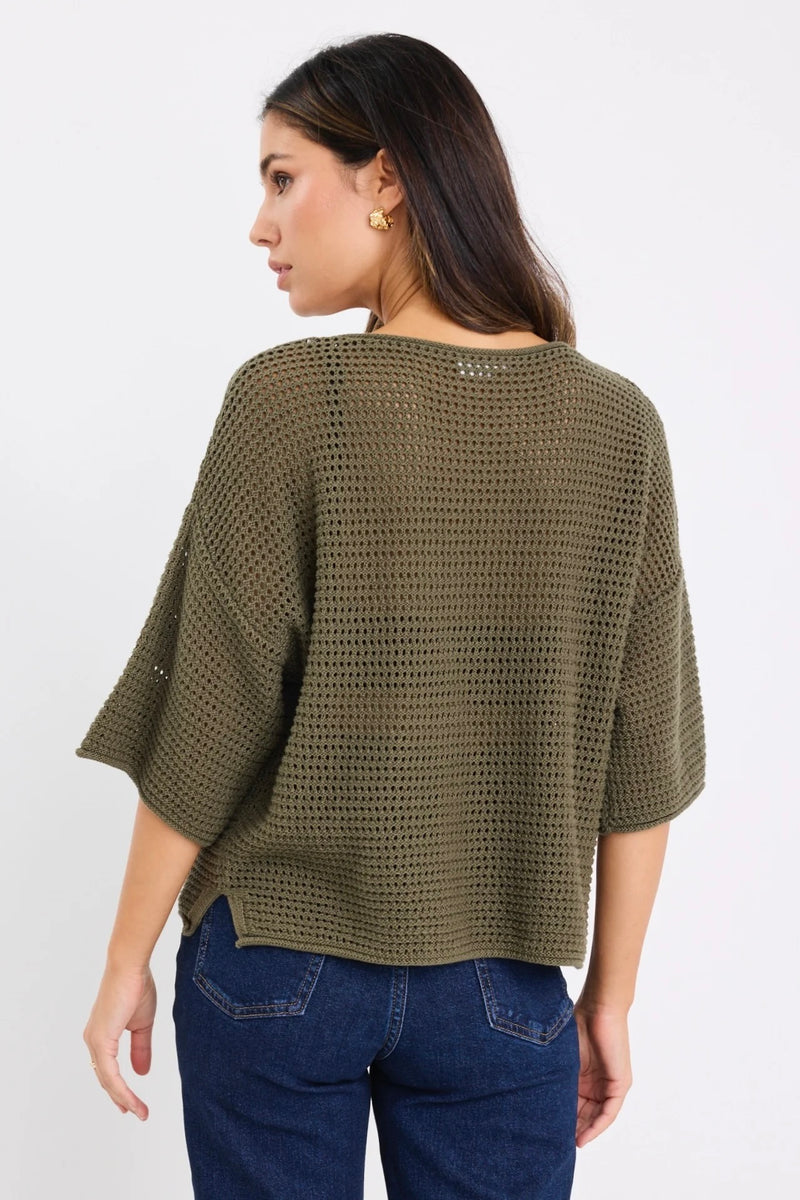 Woman wearing Re:Union The Label Sunrise Khaki SS Crochet Knit Top in crochet knit with short sleeves, relaxed fit, and round neckline, styled with denim jeans.