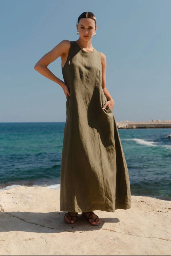 Model wearing Re:Union The Label Easygoing Khaki Linen Blend Sleeveless Crew Neck Midi Dress with relaxed fit, midi length, and side pockets, styled with sandals by the ocean