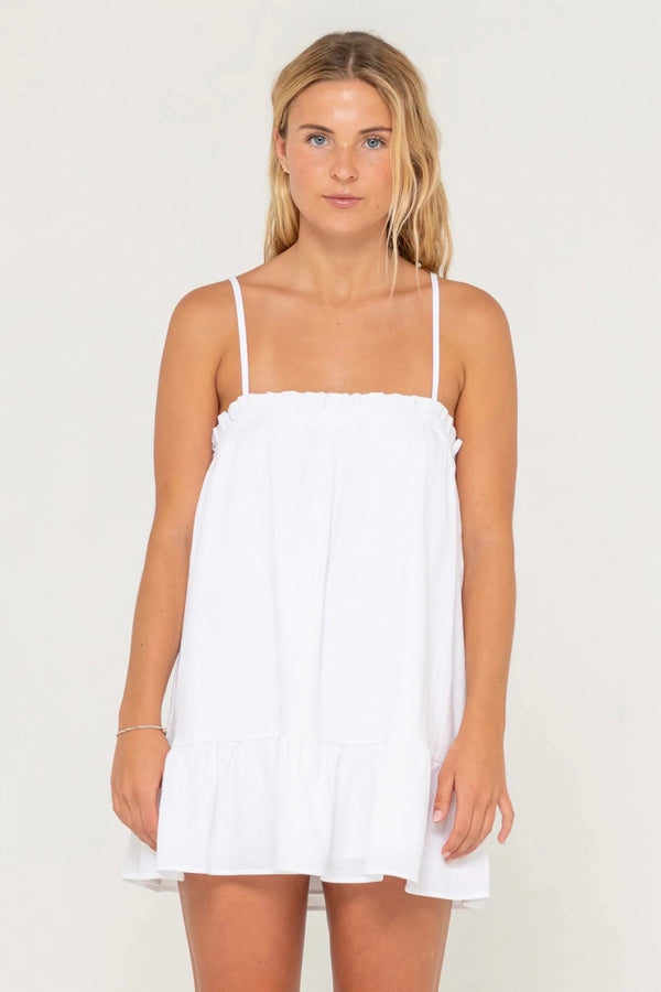 Model wearing Rusty Mary Weather Mini Dress in white with spaghetti straps and frill hem against plain background.