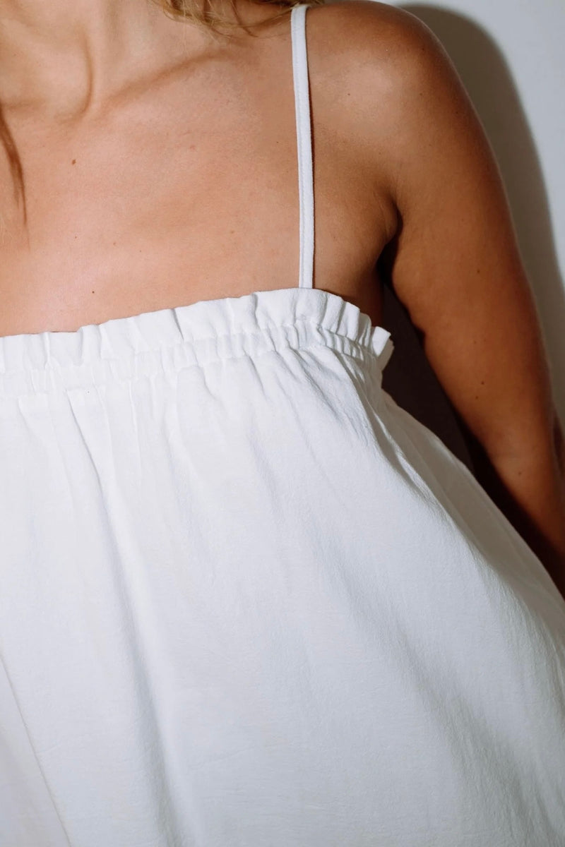 Model wearing Rusty Mary Weather Mini Dress in white with spaghetti straps and frill hem against plain background.