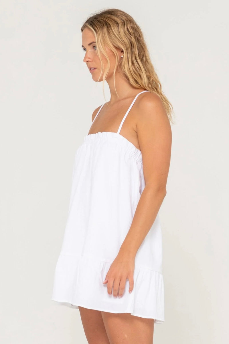 Model wearing Rusty Mary Weather Mini Dress in white with spaghetti straps and frill hem against plain background.